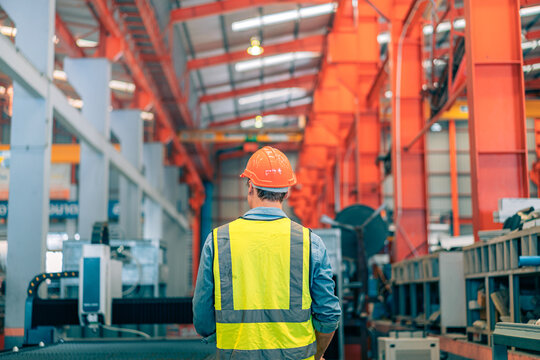 Caucasian industrial engineer man wear safety helmet vest operating CNC laser cutting machine control panel. Professional worker monitoring digital screen system. Manufacturing automation technology