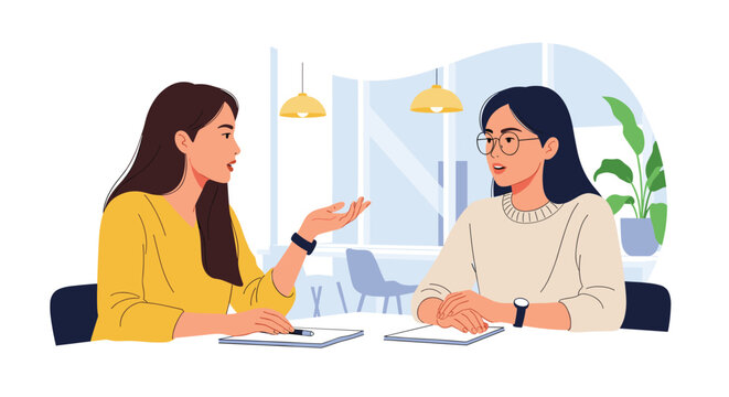 Two professional women sitting across from each other at a desk while having a serious business conversation in an office.