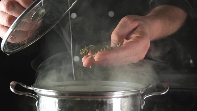 The cook adds dried herbs to a steaming pot. The kitchen is filled with the aroma of cooking food. This moment captures the process of preparing a delicious dish.