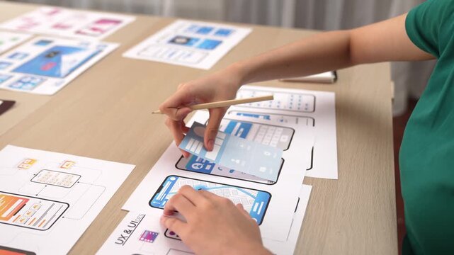 Startup company employee planning for user interface prototype for mobile application or website in office with model of program on desk. UX UI designer consider user friendly interface plan. Synergic