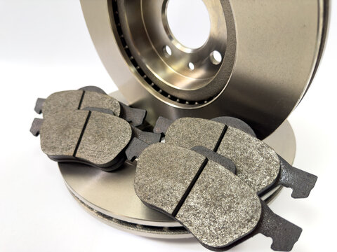 Workshop shot of brake parts arranged professionally, Detailed image of textured brake rotor and friction pads stacked neatly on workbench