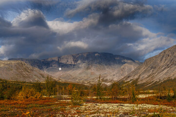 A Picturesque Mountain Valley Under a Stormy Sky with Autumn Colors and a Rare Forest Against a Mountainous Landscape