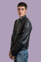 Fototapeta premium Young man wearing black leather jacket and jeans posing on purple background