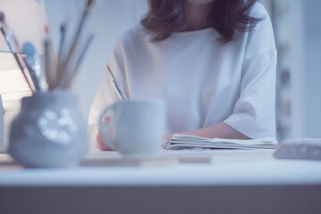 Artist drawing in a sketchbook at a minimalist white desk. Creative workspace with a single entrepreneur. Upper body shot with artistic tools
