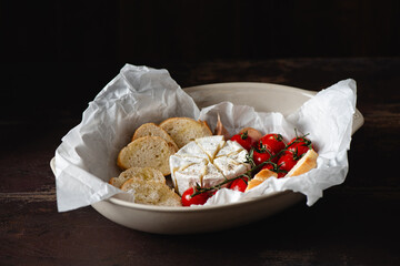 Tasty appetizer baked brie or camembert cheese with cherry tomatoes and baguette in baking dish