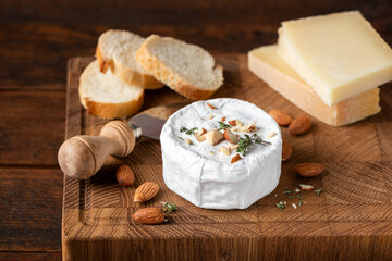 Cheese platter with brie or camembert cheese served with chopped almonds and baguette slices on wooden board