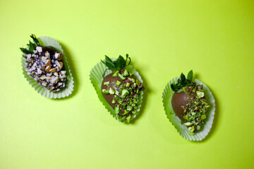 three gourmet chocolate covered strawberries with crushed nuts on a bright green background,...
