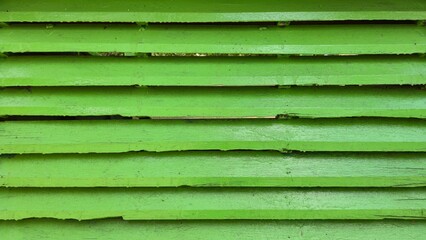  A close-up view of an old, weathered wooden wall or fence with horizontal green painted slats or planks, showing cracks and natural wood grain.