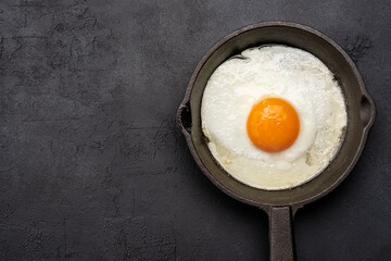 One egg cooked in a cast iron pan on black stone background