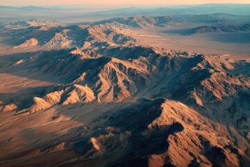 Naklejka premium Aerial view of rugged, sun-drenched mountain ranges extending across a vast desert landscape