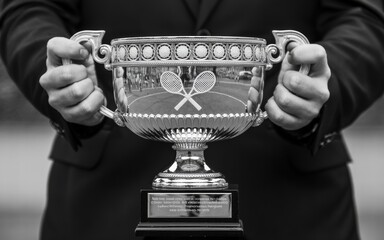 Man in suit holding a trophy cup with two handles and decorative elements