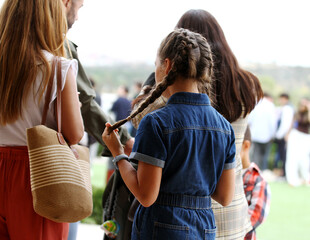 Familia y ni&ntilde;a con coleta entre personas de p&uacute;blico en plan de ocio al aire libre
