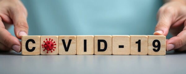 Hands form wooden cubes spelling out COVID-19 with red virus symbol. Global health crisis, pandemic awareness, medical info graphic element.