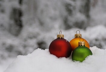 Festive glass ornaments in red, yellow, and green nestled in white snow, evoking classic winter holiday charm.