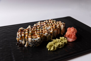 Sushi rolls topped with creamy mayonnaise and teriyaki sauce, served on a black rock