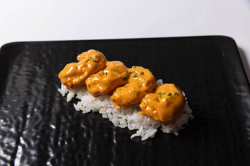 Nigiri sushi topped with crispy pieces coated in creamy spicy sauce, served on white rice on a black plate