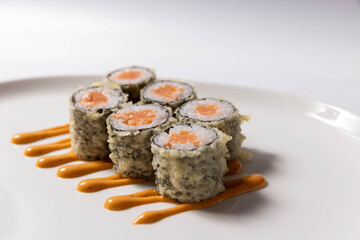 Tempura sushi rolls with crab filling served on a white plate with wasabi, pickled ginger, and creamy sauce © rilueda