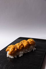 Nigiri sushi topped with crispy pieces coated in creamy spicy sauce, served on white rice