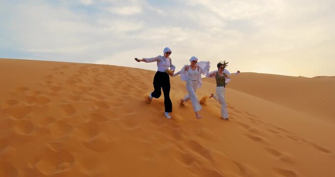Group of joyful tourist people running on desert dunes under a clear sky during a sunny day