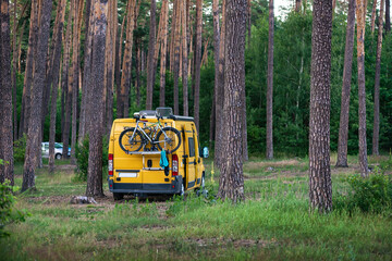 Yellow camper van with bicycles parked in a pine forest. Concept of van life, outdoor travel, freedom, eco tourism, camping and active lifestyle in nature.