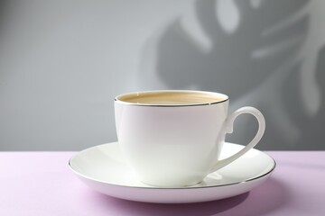 Fototapeta premium Aromatic coffee in cup on violet table, closeup