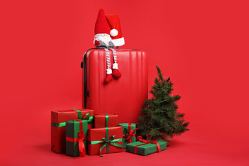 Suitcase with Santa hat, gifts, fir tree and decorative dwarf on red background. Christmas vacation