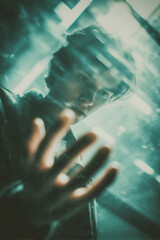 Joven con mano extendida y mirada intensa a trav&eacute;s del cristal, Retrato dram&aacute;tico en azul y verde con efecto de distorsi&oacute;n, joven adicto a redes sociales, gen z adicci&oacute;n m&oacute;vil 