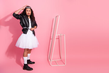 Male performer in pink studio wearing leather jacket and ballerina dress posing with mirror, celebrating pride and self expression
