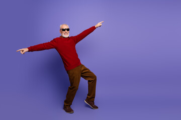 Fototapeta premium Joyful mature gentleman in red sweater dances away purple background for fashion style lifestyle advertising promotional imagery with humor and energy
