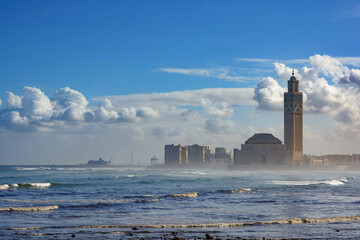 Casablanca coastline in the morning mist in autumn. Hassan II mosque can be seen across the water and a ship in the background. blue sky and clouds.