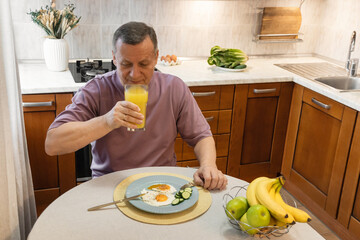 Mature man drinking orange juice and having a healthy homemade breakfast in kitchen.