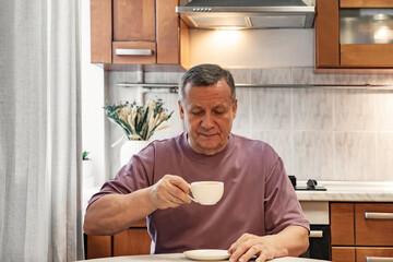 Adult man enjoying cup of coffee at kitchen table after homemade breakfast. Calm morning routine. Morning Home Cooking Making and Eating Breakfast