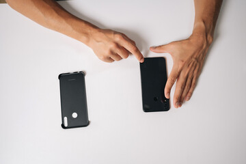 Close-up top view of technician hands inserting smartphone into protective case, ensuring secure fit sitting on white table in modern professional workshop. Concept of phone maintenance and service
