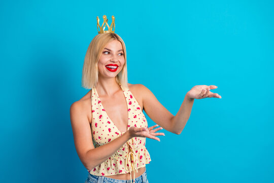 Young woman with crown smiles in floral halter top against bright blue background posing with hands