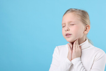 Little girl suffering from sore throat on light blue background, space for text. Cold symptom