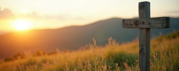 Wooden cross stands in a grassy field against a golden sunset. Hills fade into the distance under a warm sky. Light illuminates the natural landscape.