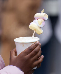Close-up of African American child hand holding cup of hot chocolate with marshmallows at Christmas market on Old Town Square in Prague, capturing winter tourism, festive shopping and street food.