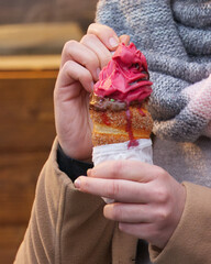 Close-up of a traditional trdelnik filled with ice cream, held by a woman at the Christmas market on Old Town Square in Prague, showing festive street food, winter atmosphere and holiday tourism.
