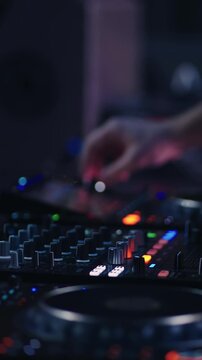 Close up of DJ mixing console with colorful lights and hand adjusting controls in dark nightclub atmosphere, electronic music performance and live party vibes