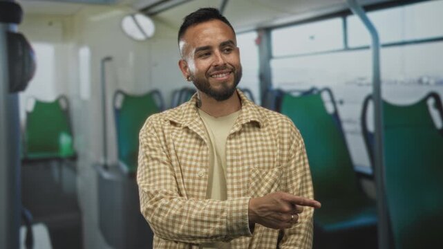 Young man finger pointing to seat inside bus on street, smiling in a plaid overshirt with earring and tattoo; friendly.