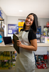 Young woman wearing apron standing in her small business, looking at camera