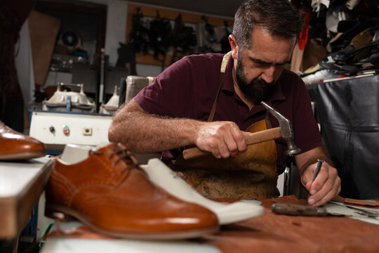 Shoemaker at work crafting leather shoes with hammer and chisel in a traditional workshop
