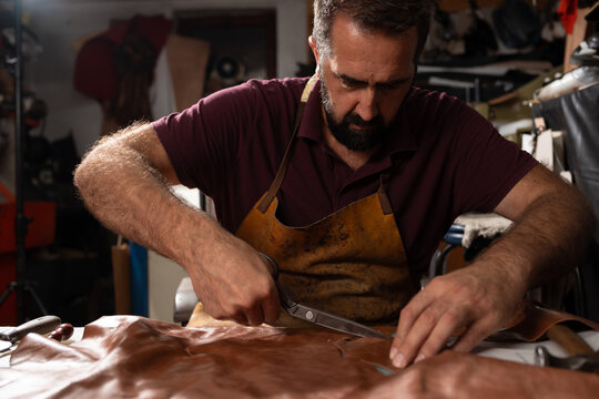 Leatherworker at a workshop cutting leather with scissors, focused artisan shaping a project