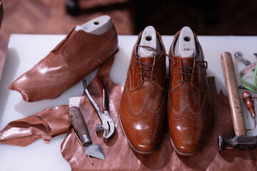 Craftsman s brown leather dress shoes with shoemaker tools laid out on a worktable.