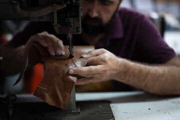 Leather work in progress: skilled craftsman sewing brown leather piece with industrial sewing machine