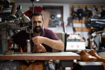 Skilled craftsman operating a sewing machine in a cluttered leather workshop making shoes