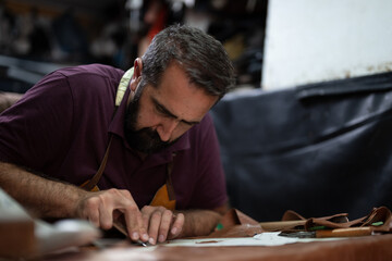 A skilled craftsman with a beard focuses on leather cutting at a workshop