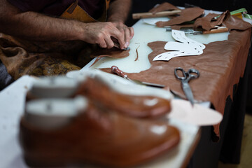 Leather crafting in progress: hands shaping brown leather with tools on a workshop table