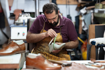 Skilled shoemaker at work measuring a leather shoe in a busy workshop