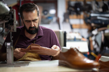 Cobbler craftsman works on leather shoes at a busy workshop, focused on stitching and finishing